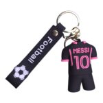 Keychain with a small black figurine wearing a pink Messi 10 jersey, attached to a strap with a soccer ball graphic and the word football on it.