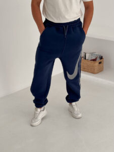 584432696_17891230356372975_2056992225192599696_n | UAE SPORT STORE Person wearing navy Nike sweatpants with a large silver swoosh, white sneakers, and a white T-shirt visible from the waist up to knees.