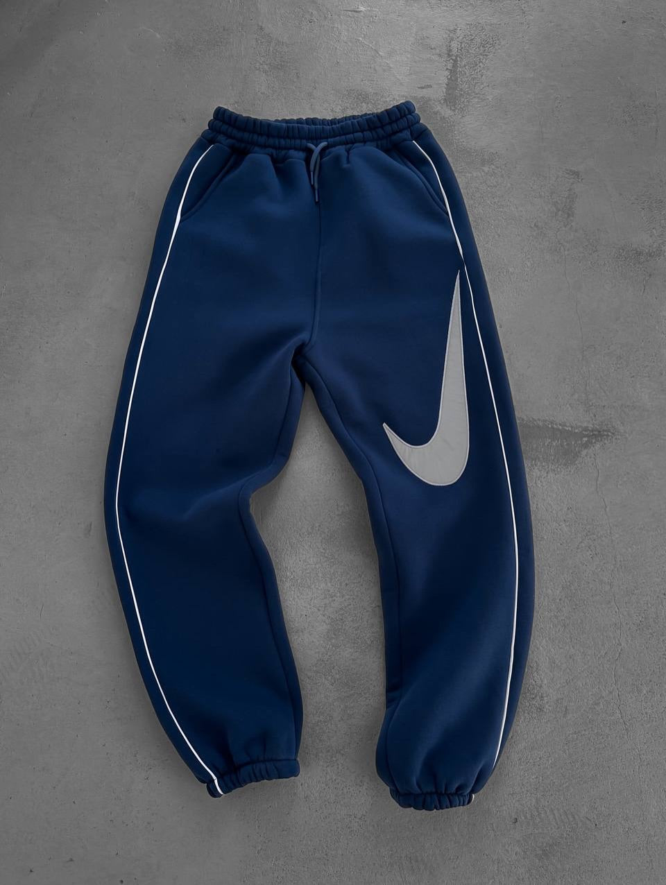 584723821_17891230338372975_971018864417932746_n | UAE SPORT STORE Navy blue Nike sweatpants with white piping along the sides and a large gray swoosh on the right leg.