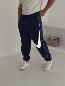 587293711_17891230329372975_4733487774298692245_n | UAE SPORT STORE Person wearing navy joggers with a large white Nike swoosh along the leg and white sneakers.