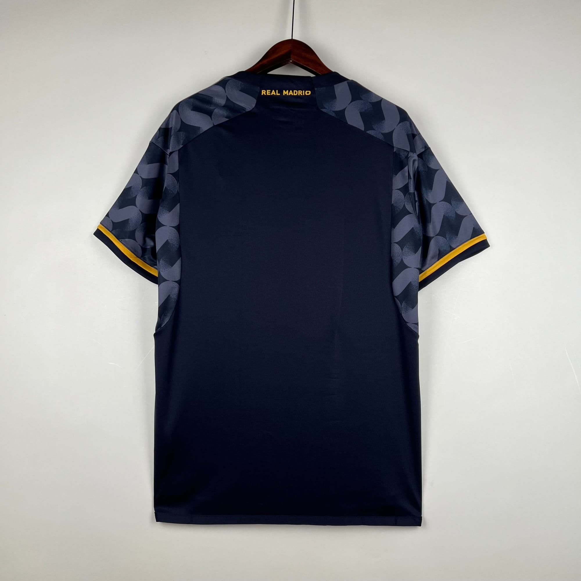 588e6572 | UAE SPORT STORE Navy shirt on a wooden hanger, back view with blue patterned sleeves, yellow trim at the cuffs, and 'REAL MADRIO' in gold on the neck area.