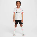 Young girl wearing Liverpool FC youth kit: white jersey with red trim, black shorts, white socks, and cleats.