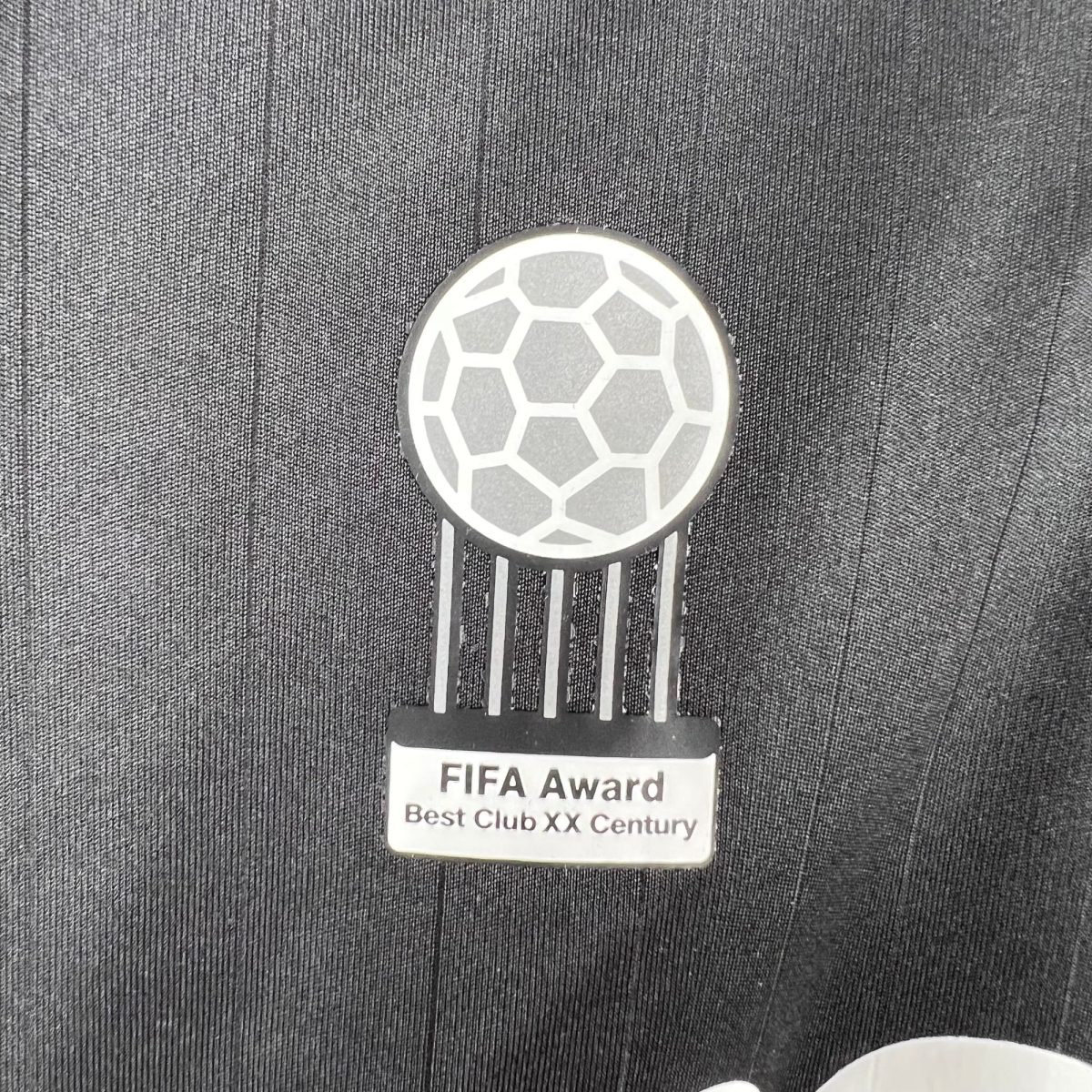 Metallic FIFA Award medal with a hexagonal soccer-ball pattern and hanging ribbons; inscription reads 'FIFA Award Best Club XX Century' (text partially visible).