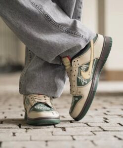 Close-up of a person wearing beige-green sneakers and baggy jeans, stepping on a cobblestone path with one foot raised.