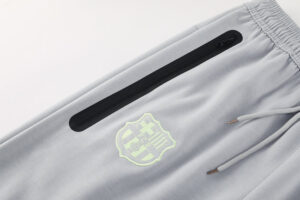 Light gray jogger pants with a black zippered pocket and a pale-green shield crest on the thigh edge.