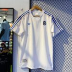594170660_1158609253088295_8025875988516450926_n | UAE SPORT STORE White Real Madrid soccer jersey with blue Adidas stripes on the shoulders and Real Madrid crest, hanging on a wooden hanger.