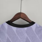 Close-up of a wooden clothes hanger with a light purple shirt hanging from a black rod against a pale wall, viewed from below.