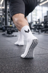 5967537890642300093 | UAE SPORT STORE Close-up of a person in a gym performing a squat, wearing white grip socks with black dots on a rubber floor.