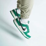 Green and white sneakers being worn while jumping against a light background