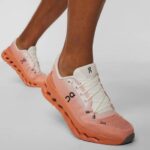 Peach-pink On running shoe with white laces on a wearer’s foot, showcasing a chunky sole.