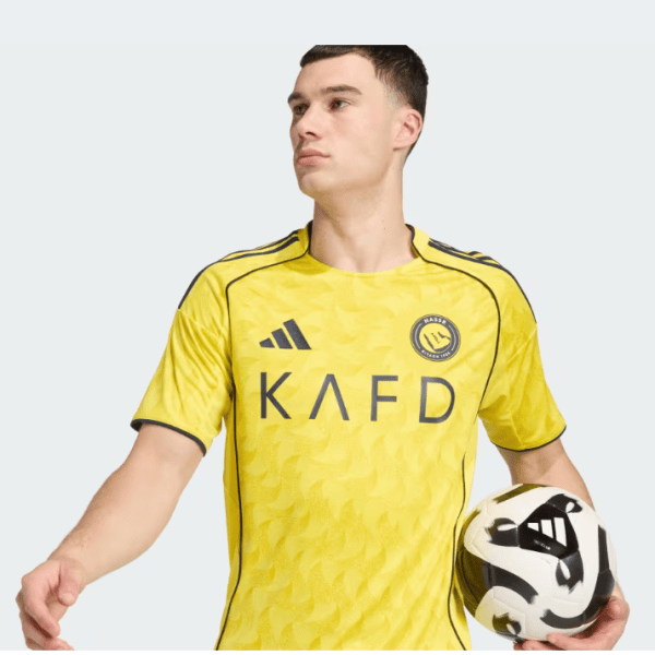 Soccer player in a bright yellow jersey holding a soccer ball at his side, facing left.