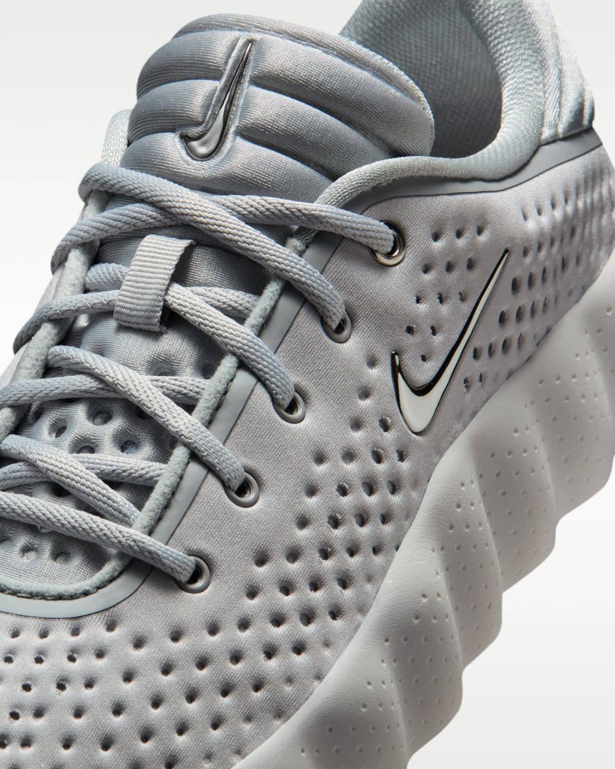 Close-up of a gray athletic shoe showing laces, perforated upper, and a black-outlined swoosh logo on the side.