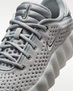 Close-up of a gray athletic shoe showing laces, perforated upper, and a black-outlined swoosh logo on the side.