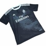 Dark Real Madrid football jersey with white shoulder stripes, crest, and Fly Emirates sponsor on a dark fabric.