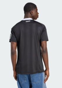 Back view of a man wearing a dark, striped soccer jersey with a white collar and RMCF logo at the neckline, paired with blue jeans against a light background.