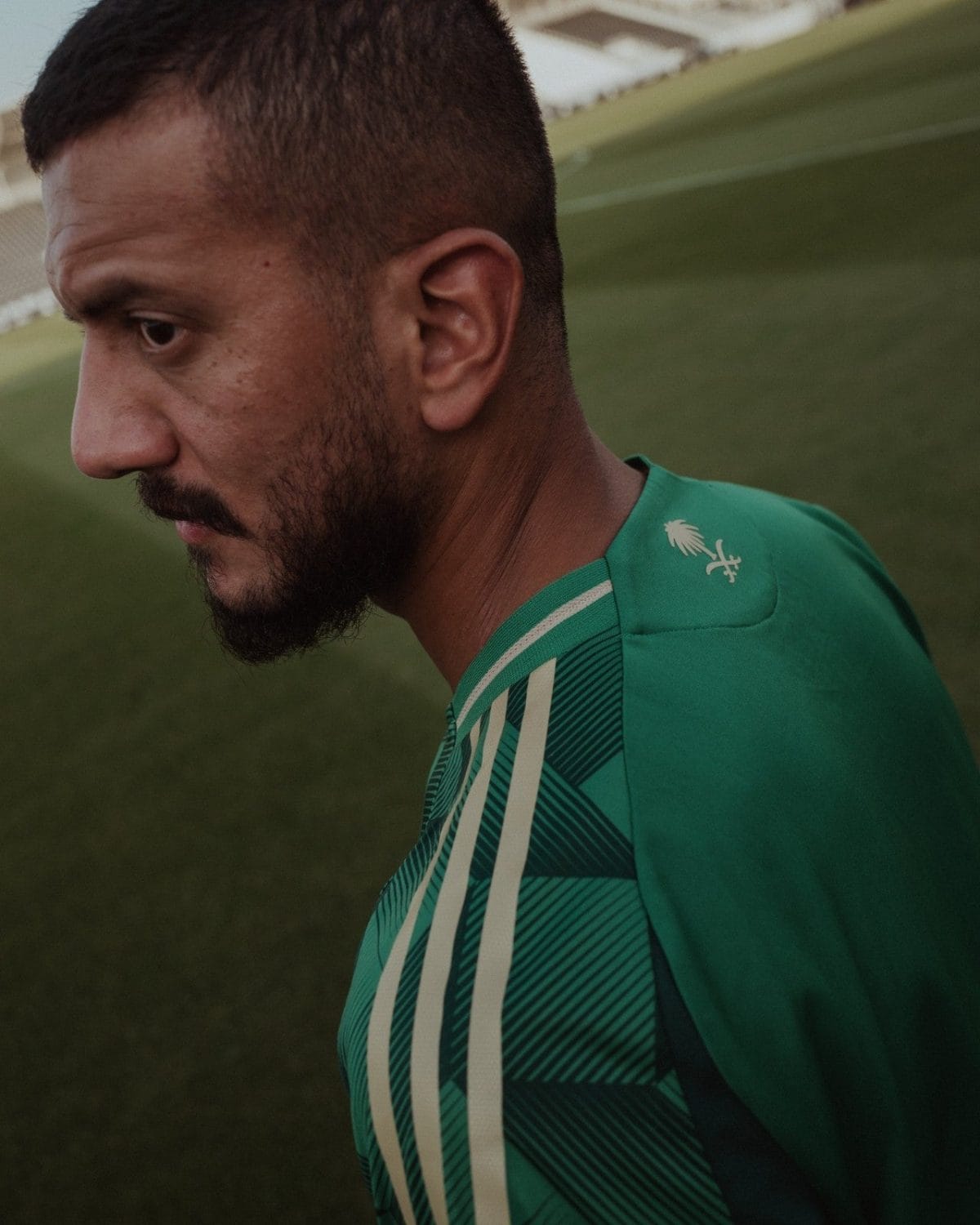 Close-up side profile of a man with a beard wearing a green sports jersey on a grassy field