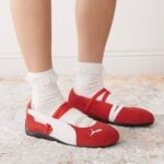 5a1f9b37-3d1b-4aa8-8715-d94d27a285ce | UAE SPORT STORE Red and white Puma sneakers with white socks on a light rug, shown from the side.