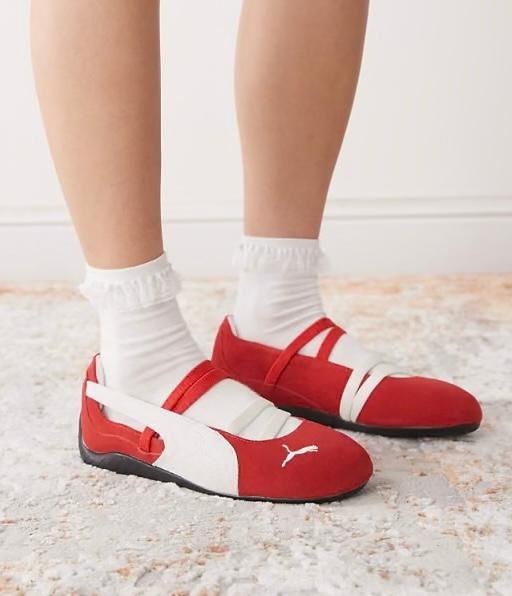 Red and white Puma sneakers with white socks on a light rug, shown from the side.