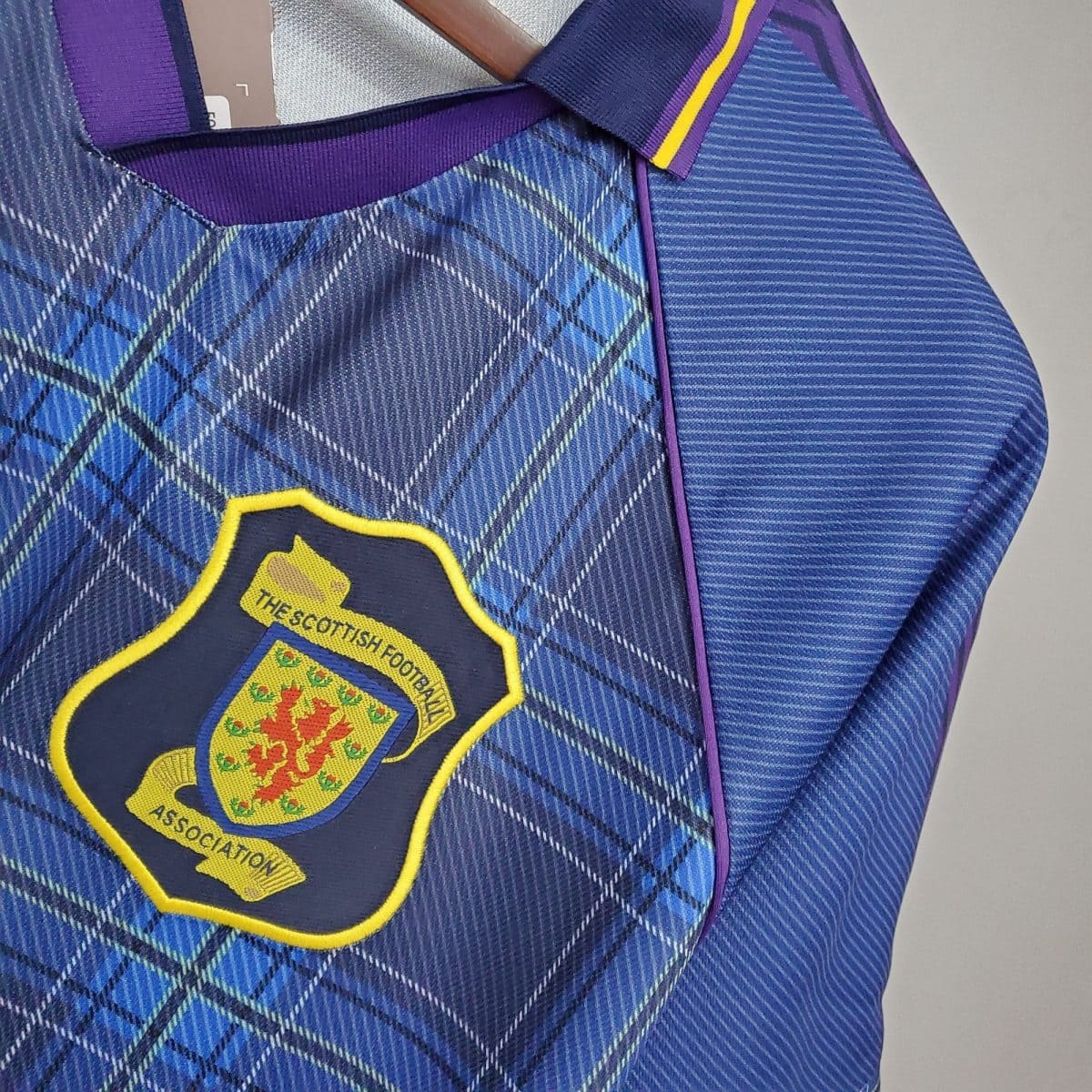 Close-up of a blue plaid jersey with a purple collar and a yellow-edged shield badge reading 'The Scottish Football Association'.