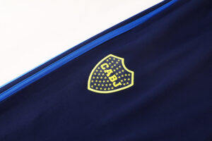 5aa5c063 | UAE SPORT STORE Navy fabric with a yellow shield-shaped logo filled with stars and the letters 'CABJ' in the center, near a blue seam edge.