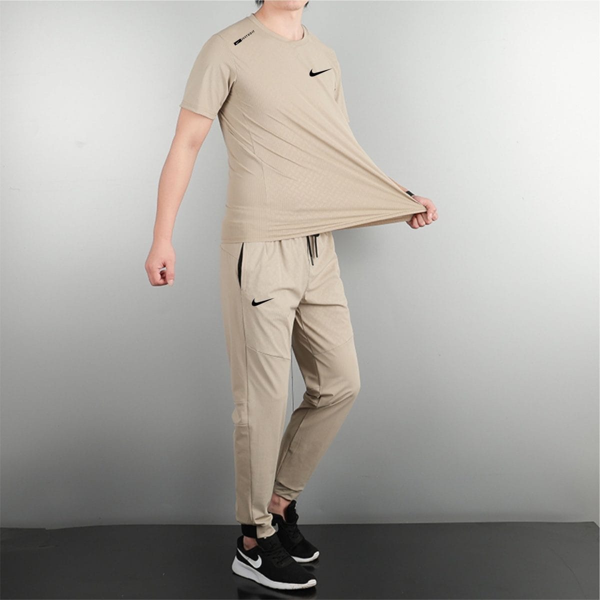 Person wearing a beige athletic outfit and black Nike sneakers, standing in a studio.