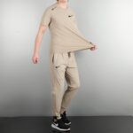 Person wearing a beige athletic outfit and black Nike sneakers, standing in a studio.