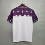 Back of a purple patterned sports jersey on a hanger, with a jagged white transition to a white body on the lower half.