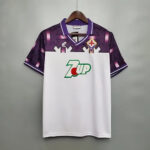 Fiorentina football jersey on a hanger with purple zigzag shoulders, white front, club crest, and 7UP sponsor logo.