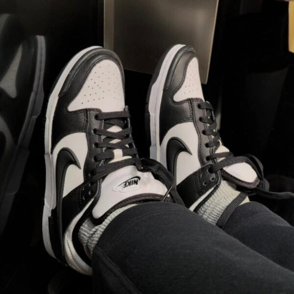 Person wearing black-and-white Nike sneakers with black laces, feet crossed and resting on a surface, showing the Nike swoosh on both shoes.