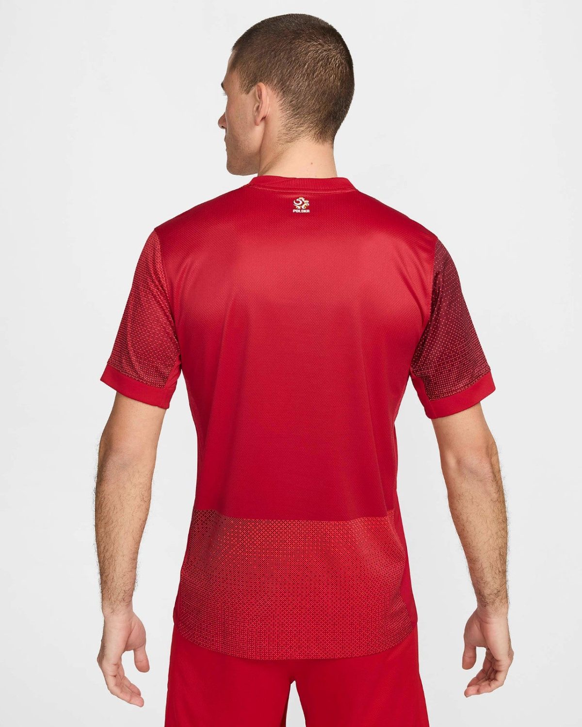 Back view of a man wearing a red athletic shirt with mesh panels on sleeves and lower back; small white logo at the nape.