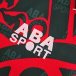 5bb018d0_272b0e30-cc6f-4178-bd5a-dd5e643f499b | UAE SPORT STORE Close-up of red and dark fabric with bold white letters partially visible. Textured textile surface with printed pattern.