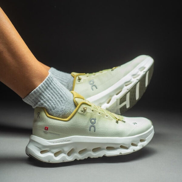 athletic runner's light-green sneakers with yellow trim and gray socks, mid-run on a dark background