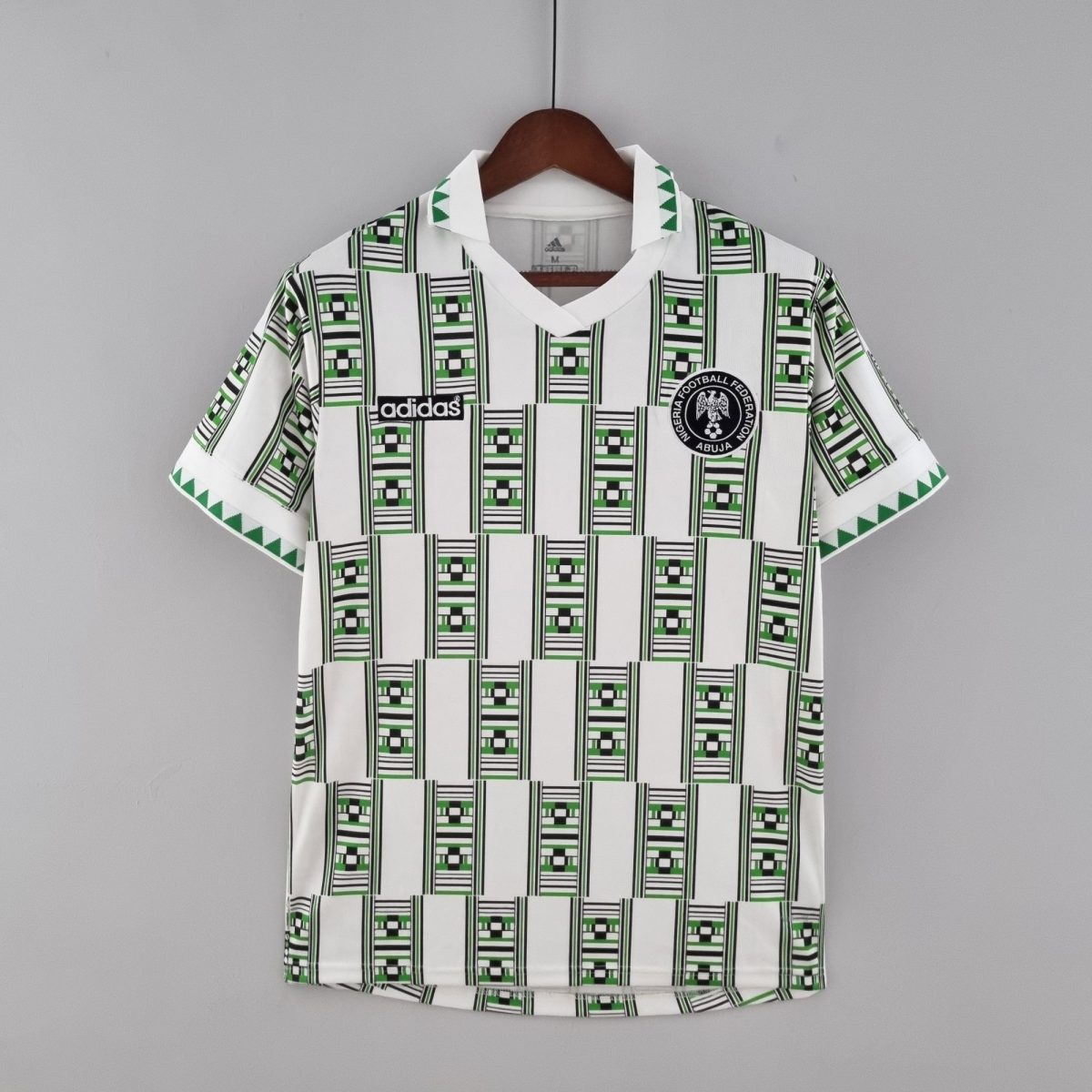 White football jersey on a wooden hanger with black-and-green geometric stripes, featuring Adidas logo and Abuja Football Federation badge in front.
