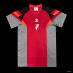 5c10faeb7ad54e3831c7c2e1 | UAE SPORT STORE Red and gray Adidas soccer jersey with a red central panel, gray sides, and black/orange shoulder accents, featuring a white club crest on the chest.