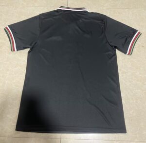 Back view of a black polo shirt laid flat, featuring green, white, and red striped trim on the collar and sleeve cuffs.