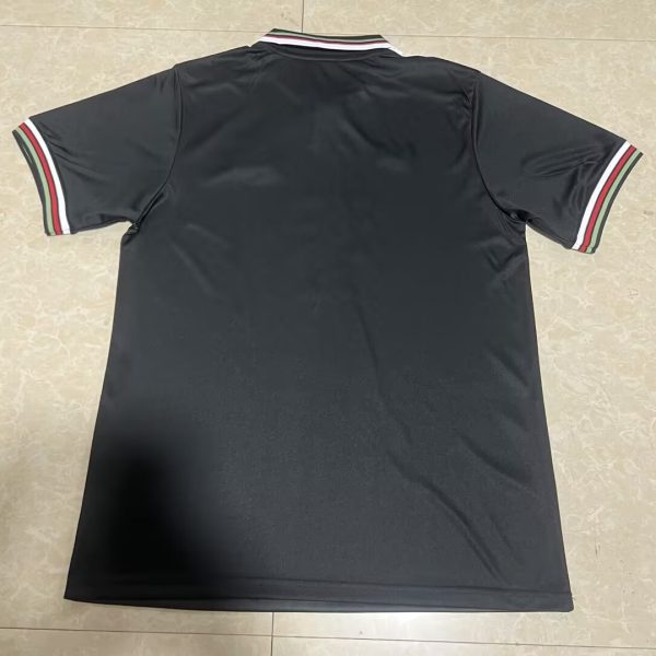Back view of a black polo shirt laid flat, featuring green, white, and red striped trim on the collar and sleeve cuffs.