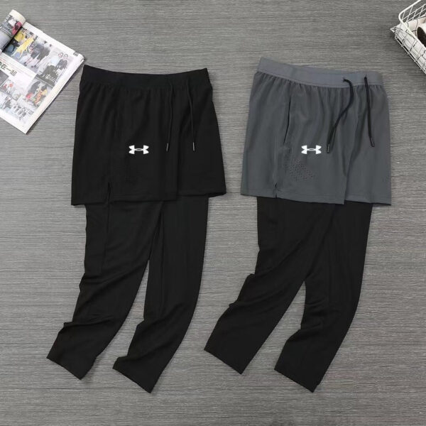 Two sets of athletic shorts laid flat on a gray floor: black shorts with black leggings, and gray shorts over black leggings, both with drawstrings and UA logo.