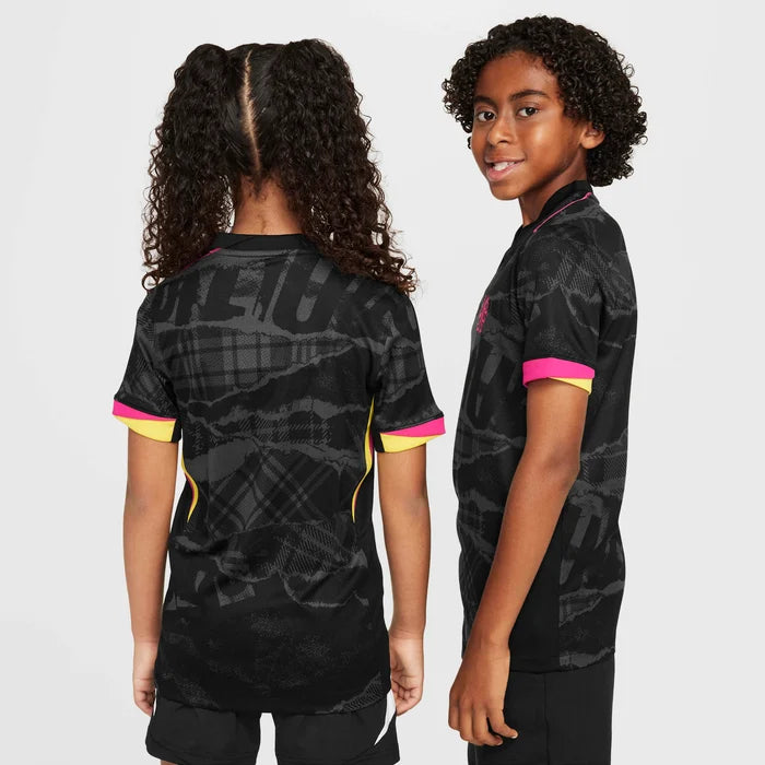 5d30666c_6c58_4708_a301_1c4bdc776710 | UAE SPORT STORE Two children showing the back and side of black graphic athletic jerseys with pink cuffs and yellow trim against a gray background, kid-focused fashion photo