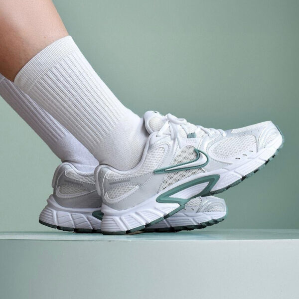 Person wearing white running shoes with teal accents and white ribbed socks stepping on a pale green surface.