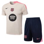 Beige FC Barcelona soccer jersey with pink shoulder detail and navy Nike swoosh, large circular sponsor logo, paired with navy shorts featuring the pink Barça crest.