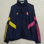 5d5845691508bd18 | UAE SPORT STORE Navy windbreaker with Adidas logo on left chest and pink flamingo emblem on right; yellow diagonal stripe on left sleeve and pink accents on right sleeve.