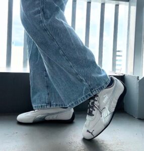 Close-up of a person in blue jeans stepping onto a balcony ledge, wearing white Puma sneakers with black soles.