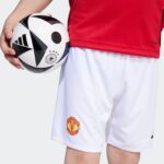 A child holding a soccer ball against a red jersey and white shorts featuring the Manchester United crest.