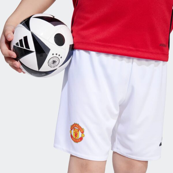 A child holding a soccer ball against a red jersey and white shorts featuring the Manchester United crest.