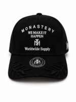 Black baseball cap with white embroidery reading 'MONASTERY WE MAKE IT HAPPEN Worldwide Supply' and a circular logo on the front panel, plus decorative stitched leaves on the brim's sides.
