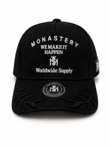 Black baseball cap with white embroidered text reading 'MONASTERY WE MAKE IT HAPPEN Worldwide Supply' and a circular logo on the brim patch.