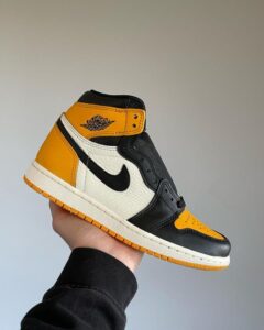 Hand holding a high-top Air Jordan 1 sneaker in black, white, and yellow colors.