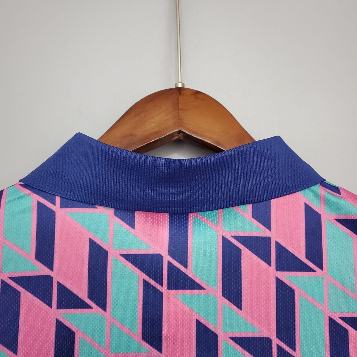 Close-up of a geometric-patterned shirt on a wooden hanger, showing a blue collar and pink/teal/navy shapes.