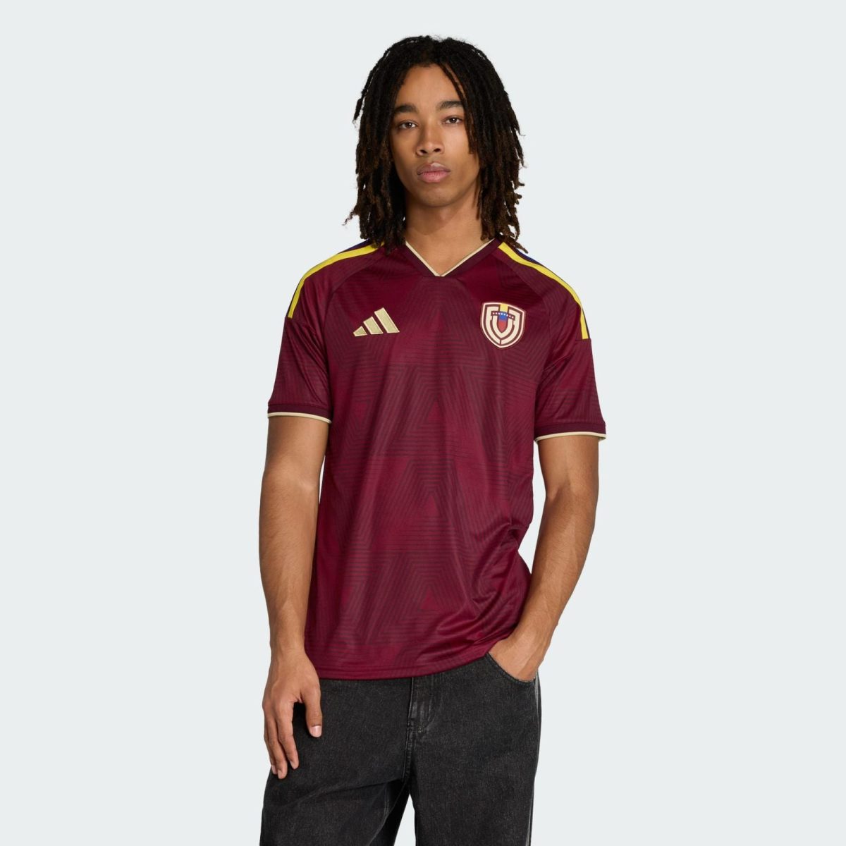 Adult wearing maroon soccer jersey with crest and Adidas logo, standing against a light background.