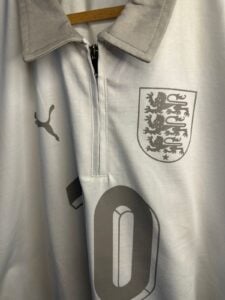 Light gray athletic jacket with a half-zip, displaying a crest featuring three lions on the chest and a Puma logo on the left sleeve area; fabric hanger visible in background.